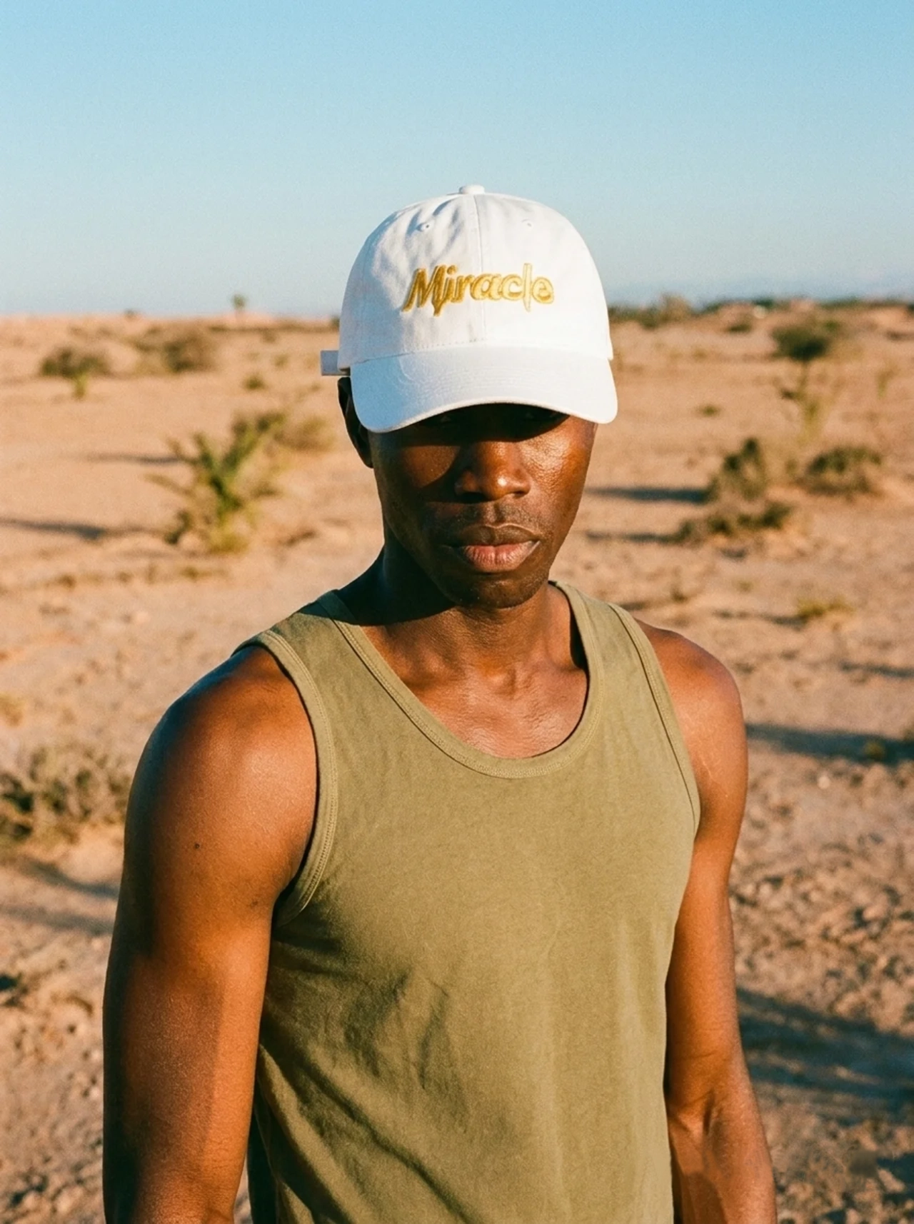 Person wearing a white cap with 'Miracle' logo and green tank top in a desert setting
