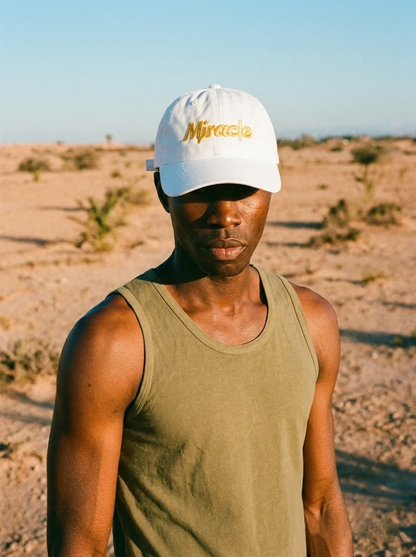 Person wearing a white cap with 'Miracle' logo and green tank top in a desert setting